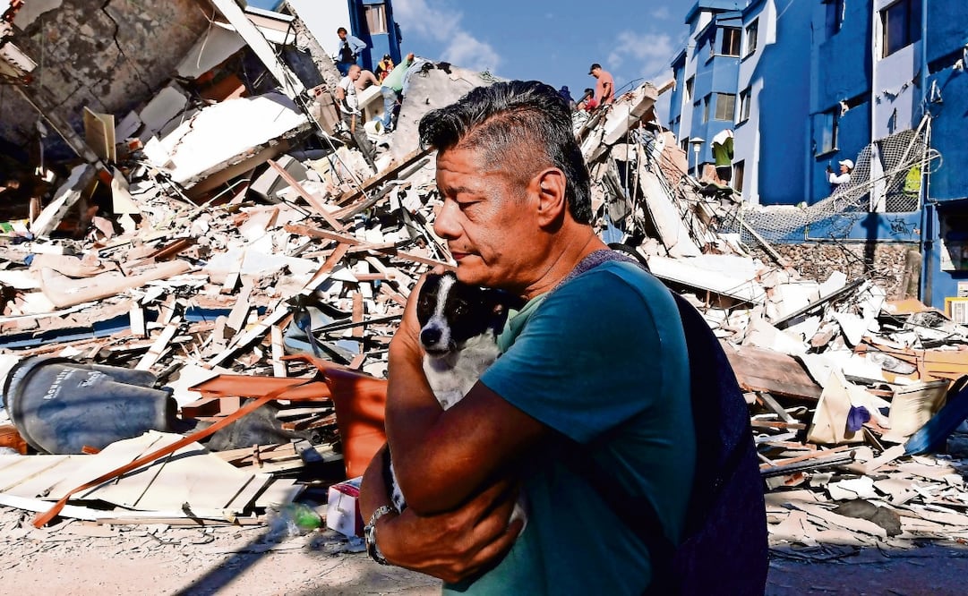 Un hombre con un perro en brazos pasa junto a los escombros de un edificio derrumbado en Pereira. Foto: AFP